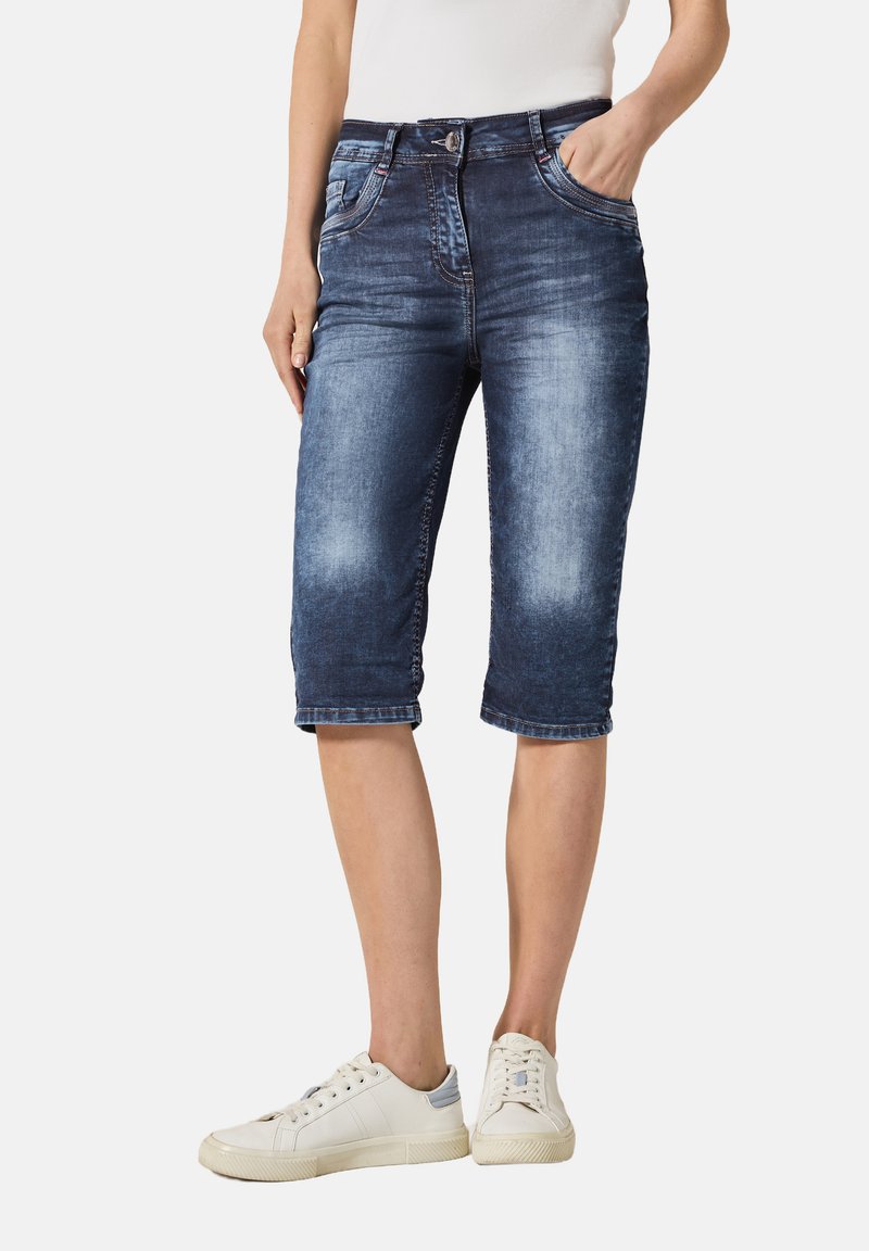 Capris en jean bleu foncé avec une finition délavée, cinq poches et ourlets retroussés. Associés à des baskets blanches pour un look décontracté.