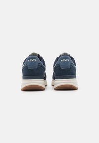 Zilā jūras krāsas sporta apavi ar zamša un sieta augšdaļu, balts vidusmērs un gumijas zole. Iespējas: Levi's logo uz papēža un kontrastējošas akcenti.