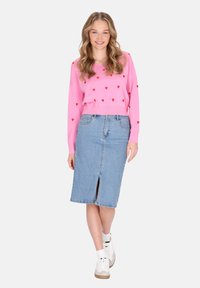 Rosa Langarmpullover mit roten Herzmustern, kombiniert mit einem hellblauen Jeansrock mit Schlitz vorne. Weiße Sneaker rundeten das Outfit ab.