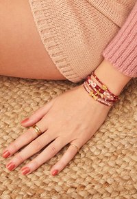 Ensemble de bracelets colorés aux textures variées, y compris des designs tressés et perlés. Main ornée de bagues en or et de vernis à ongles corail.