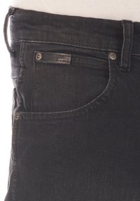 Jeans de mezclilla negra con un diseño ajustado, estilo de cinco bolsillos y una pequeña etiqueta de marca cerca de la cintura con detalles en metal plateado.