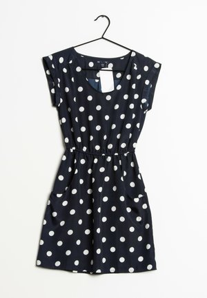 Laivastonsininen mekko, jossa valkoiset pilkut, lyhyet hihat, joustava vyötärö ja sivutaskut, roikkuu mustassa henkariin valkoista taustaa vasten.