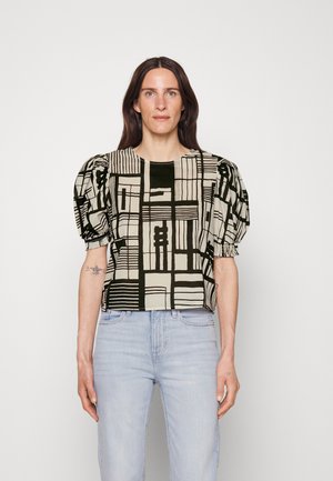 Blouse à manches bouffantes en tissu à motifs, présentant des designs géométriques noirs et beiges. Coupe courte, décolleté rond et bords de manches froncés.