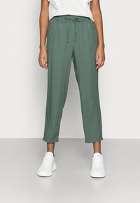 Pantalones verdes, ligeros y de corte relajado con cintura elástica y cordón. Presentan perneras rectas y textura suave. Combinados con zapatillas blancas.