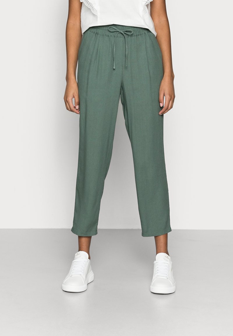 Pantalones verdes, ligeros y de corte relajado con cintura elástica y cordón. Presentan perneras rectas y textura suave. Combinados con zapatillas blancas.
