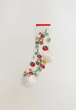 Balta kojinė su raudonu kraštu, dekoruota vaisių vynmedžio motyvu su raudonais, geltonais, žaliais ir ruda akcentais, pagaminta iš minkštos, pintos tekstūros.