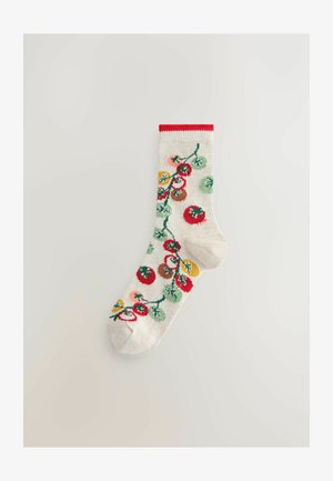 Balta kojinė su raudonu kraštu, dekoruota vaisių vynmedžio motyvu su raudonais, geltonais, žaliais ir ruda akcentais, pagaminta iš minkštos, pintos tekstūros.