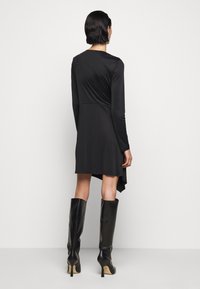 Schwarzes langärmeliges Kleid mit tailliertem Oberteil, ausgestelltem Saum und asymmetrischem Schnitt. Kombiniert mit kniehohen schwarzen Lederstiefeln und eleganten Designdetails.
