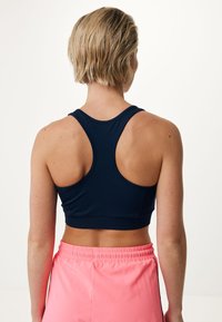 Sujetador deportivo azul marino con diseño de espalda nadadora, textura suave y silueta ajustada. Combinado con pantalones cortos rosas que cuentan con una cinturilla elástica.