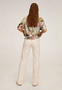Chemise à manches courtes à motif floral sur fond bleu clair, ornée de feuilles vertes et de fleurs roses, associée à un pantalon large crème.