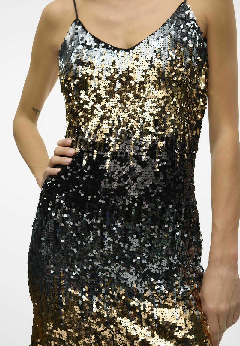 Sukienka z cekinami z gradientem przechodzącym od czerni do złota. Materiał jest błyszczący, ma dekolt w serek oraz cienkie ramiączka, co tworzy dopasowaną sylwetkę.