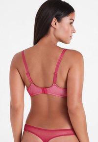 Roze mesh lingerie set met een bh met verstelbare bandjes en een haak-en-oogsluiting, gecombineerd met bijpassende lage slipjes.