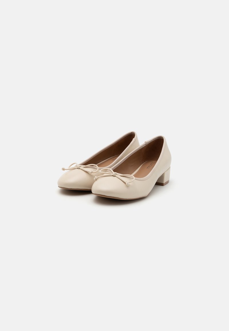 Ballerines en cuir beige avec un petit talon carré, un bout pointu et un nœud décoratif avec des perles sur le devant.