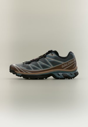 Une chaussure de trail Salomon grise et marron, avec une semelle noire robuste, présentée de profil sur un fond uni.