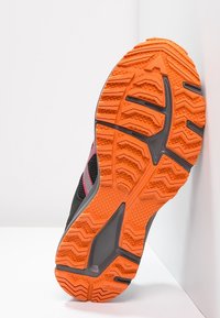 Semelle de chaussure de sport noire avec un motif de semelle robuste orange. Présente des accents gris et des rayures roses. Tige en mesh léger visible sur les côtés.