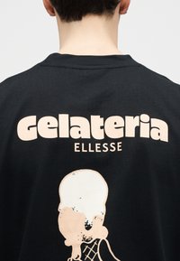 Άτομο που φοράει μαύρο πουκάμισο με τα κείμενα "gelateria" και "ellesse" πάνω από ένα γραφικό παγωτού στην πλάτη.