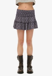 Lila gemusterter Minirock mit Rüschensaum, versehen mit weißen kreisförmigen Designs und Seitentaschen, kombiniert mit braunen Leder-Stiefeletten.