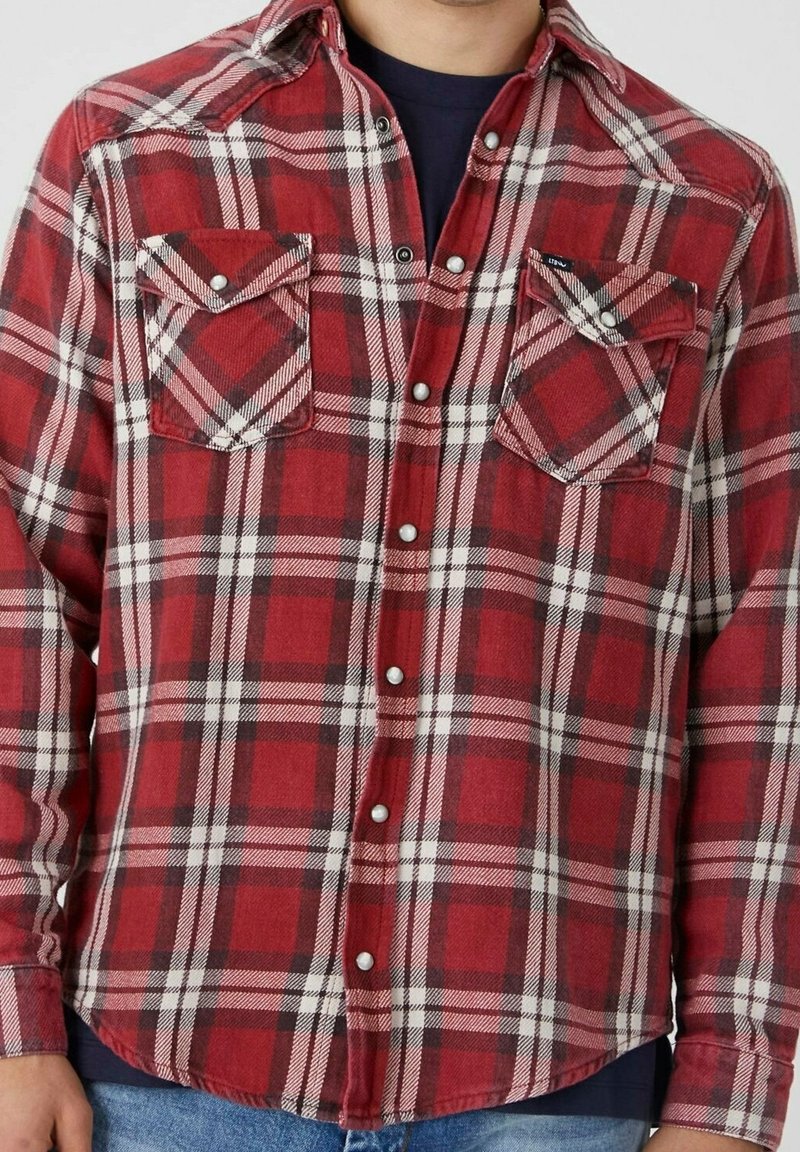 Chemise en flanelle à carreaux rouges et blancs avec un devant à boutons, dotée de deux poches poitrine, d'un ourlet arrondi et d'une texture douce.