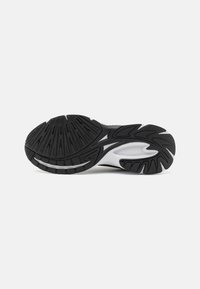 Semelle de chaussure de sport noir et blanc avec un motif texturé, comportant de profonds sillons et une section centrale lisse pour une meilleure adhérence.