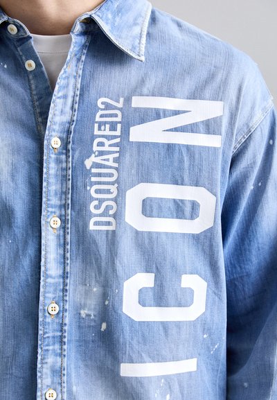 Vaaleansininen farkkupaita, jonka etuosassa on valkoiset printtitekstit "DSQUARED2 ICON", klassinen kaulus ja napitus.