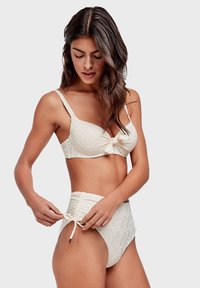 Witte bikini set met een geknoopt bustier top en hooggesneden onderkant met een gestructureerd cirkelpatroon. Verstelbare strikjes aan de zijkanten.