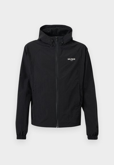 Chaqueta ligera negra con cierre de cremallera en la parte delantera, capucha ajustable, puños elásticos y detalle del logo en el pecho. Textura suave y diseño minimalista.