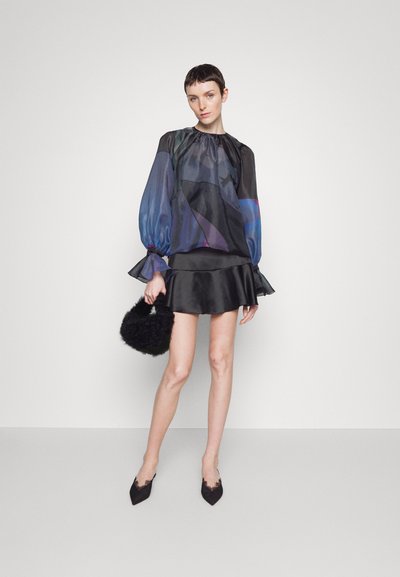 Blouse noire transparente avec des motifs géométriques bleus et violets, associée à une mini-jupe en satin noir et un sac à main en fourrure noire. Talons aiguilles.
