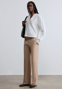 Λευκό βαμβακερό μπλουζάκι με V-λαιμόκοψη, φαρδιά μακριά μανίκια, συνδυασμένο με μπεζ παντελόνι με ψηλή μέση και μαύρα επίπεδα παπούτσια. Περιλαμβάνεται μαύρη τσάντα.