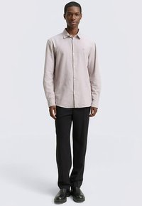 Világos rózsaszín, gombos ing puha anyagból, hosszú ujjakkal és klasszikus gallérral, fekete szabott nadrággal és fekete cipővel párosítva.