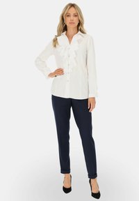 Biała bluzka z długim rękawem z falbaną z przodu i zapięciem na guziki, zestawiona z granatowymi spodniami slim-fit i czarnymi szpilkami.