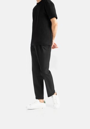 T-shirt noire à manches courtes associé à un pantalon noir et des baskets blanches avec des accents verts. Design minimaliste, texture lisse.
