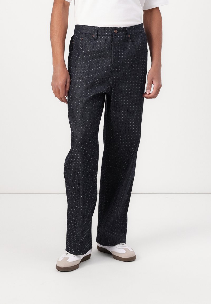 Mørke denimbukser med løs passform, med prikkete mønster, knappelukking og fem lommer. Kombinert med hvite og beige sneakers.