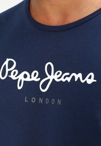 Mörkblå t-shirt i mjukt tyg med vit kursiv text "Pepe Jeans" och "LONDON" i mindre grå bokstäver under.