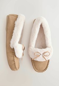 Tan suede slippers with white faux fur lining, featuring a rounded toe and a bow detail. The outsole is flat and textured for grip.