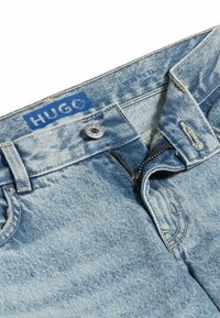 Ljusblå denimjeans med en urblekt textur, med en HUGO-etikett, metallknapp och dragkedja. Detaljer inkluderar sydda accenter och fickor.