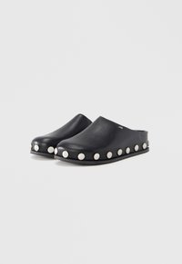 Black leather clogs with a smooth finish and rounded toe. Features silver studs along the sole and a flat, textured rubber outsole.