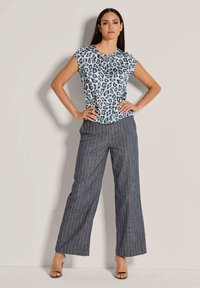 Lichtblauwe top met zwart luipaardprint, geplooide halslijn; grijs gestreepte wijde broek, gedragen met zwarte hakken met bandjes.