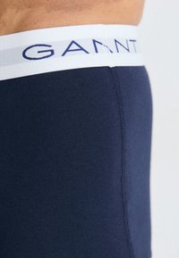 Mørkeblå boksershorts laget av elastisk bomull, med en hvit midjebånd med blå "GANNI"-logo. Glatt tekstur og tettsittende design.