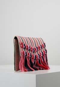 Borsa a tracolla intrecciata con un motivo a righe nei colori rosa, blu navy e crema. Presenta delle frange testurizzate lungo il bordo inferiore. Forma rettangolare.