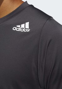Černé sportovní tričko vyrobené z hladkého, elastického materiálu. Má bílé logo Adidas na rameni a jednoduchý design s kulatým výstřihem.
