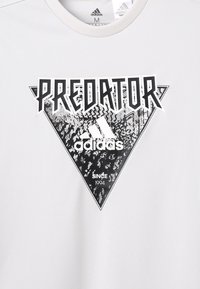 Camiseta gris de manga corta con un gráfico triangular en blanco y negro que presenta el texto "PREDATOR" y el logo de Adidas. Textura suave.