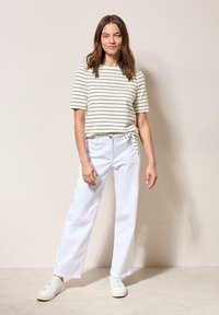 Gestreepte, lichtgroene T-shirt met een geknoopte detail aan de zijkant, gecombineerd met witte rechte jeans en witte sneakers.