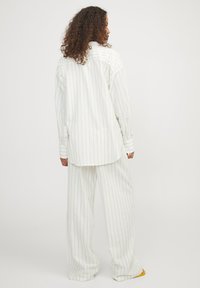 Camisa de gran tamaño a rayas blancas y pantalones anchos a juego, con sutiles rayas doradas y un ajuste relajado, confeccionados en una tela suave.