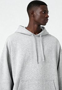 Pelēka kapučjaka ar faktūru, pārāk liela izmēra, ar auklām apkaklē un priekšējo kabatu.