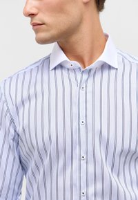 Camicia a righe blu e bianche, in cotone, con colletto bianco, chiusura frontale con bottoni discreti e finitura strutturata.