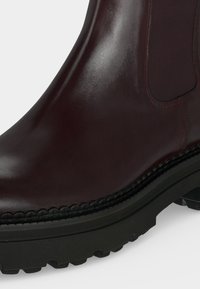 Gros plan d'une botte en cuir marron foncé avec un panneau latéral élastique et une semelle épaisse noire à crampons.