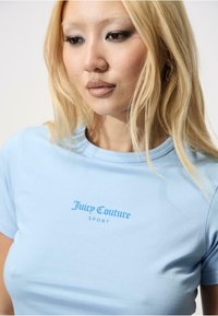 Világoskék Juicy Couture Sport póló, rövid ujjú, kerek nyakú, pamut anyagból készült, sötétebb kék logóval a mellkasán.