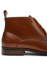 Brown leather ankle boot with a smooth finish, rounded toe, and decorative stitching. Features a contrasting wood-like sole and pull tab.