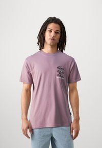 Camiseta de algodón morada con un diseño gráfico de olas y montañas en el lado izquierdo del pecho. Mangas cortas, cuello redondo, corte relajado.