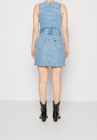 Jeansklänning med en figursydd överdel, insydd midja och vid kjol. Ljusblå färg, synlig sömnad och två bakfickor. Svarta klackstövlar.